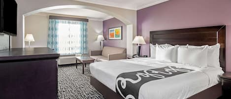 A hotel room with a large bed, a desk, a chair, and a television.