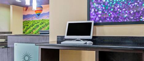 A reception desk with a computer monitor, a printer, and a decorative wall with a grapevine mural and hot air balloons.