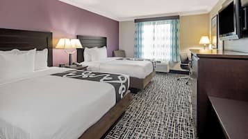 A hotel room with two beds, a desk, a TV, and a window with patterned curtains.