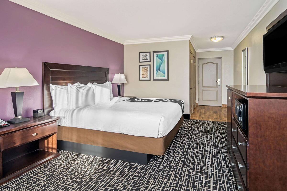 A hotel room with a large bed, a desk with a lamp, a dresser, and a TV.