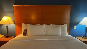 Une chambre d’hôtel avec un grand lit, une tête de lit en bois, deux lampes de chevet et une table de chevet avec une lampe et un téléphone.