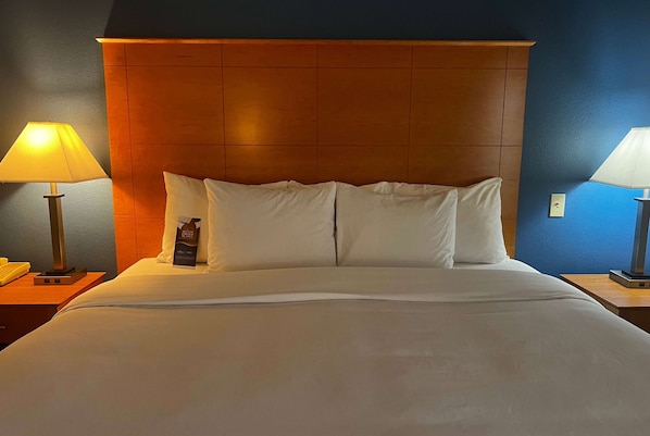 Una habitación de hotel con una cama grande, cabecera de madera, dos lámparas de noche y una mesita de noche con lámpara y teléfono.