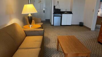 A compact living space with a sofa, a round table with a lamp, a small kitchenette, and a patterned carpet.