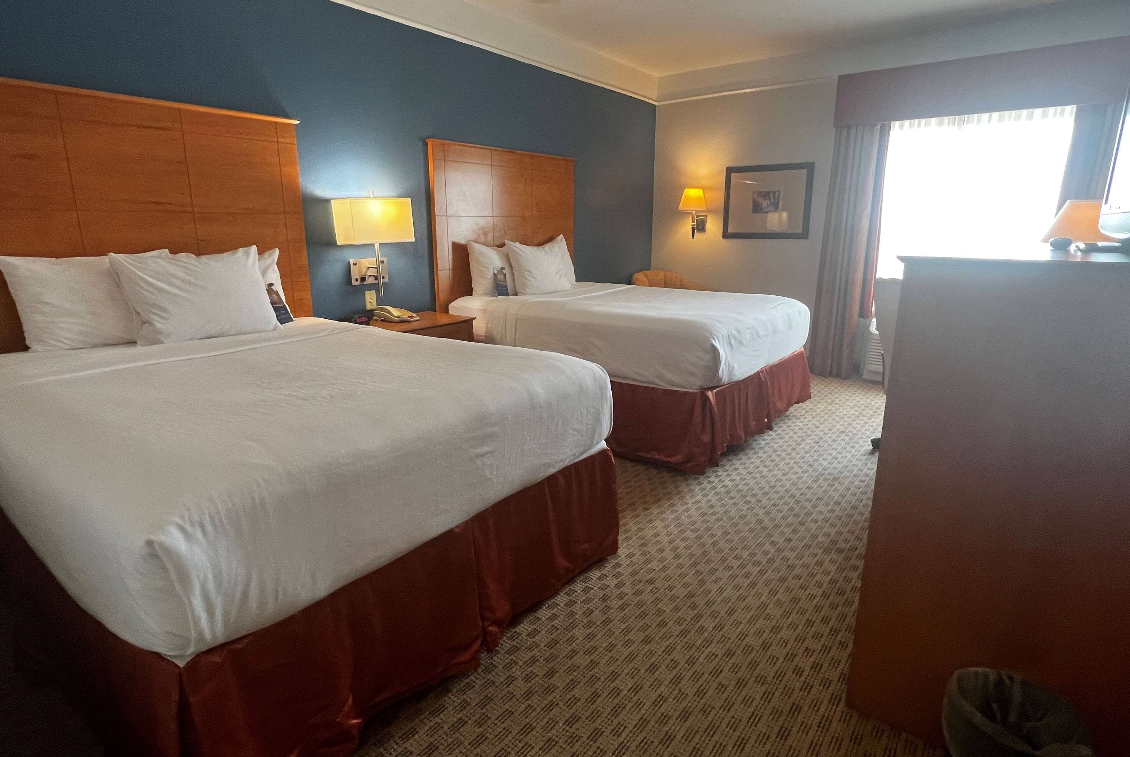 Une chambre d’hôtel avec deux lits, un bureau, une lampe et une fenêtre.