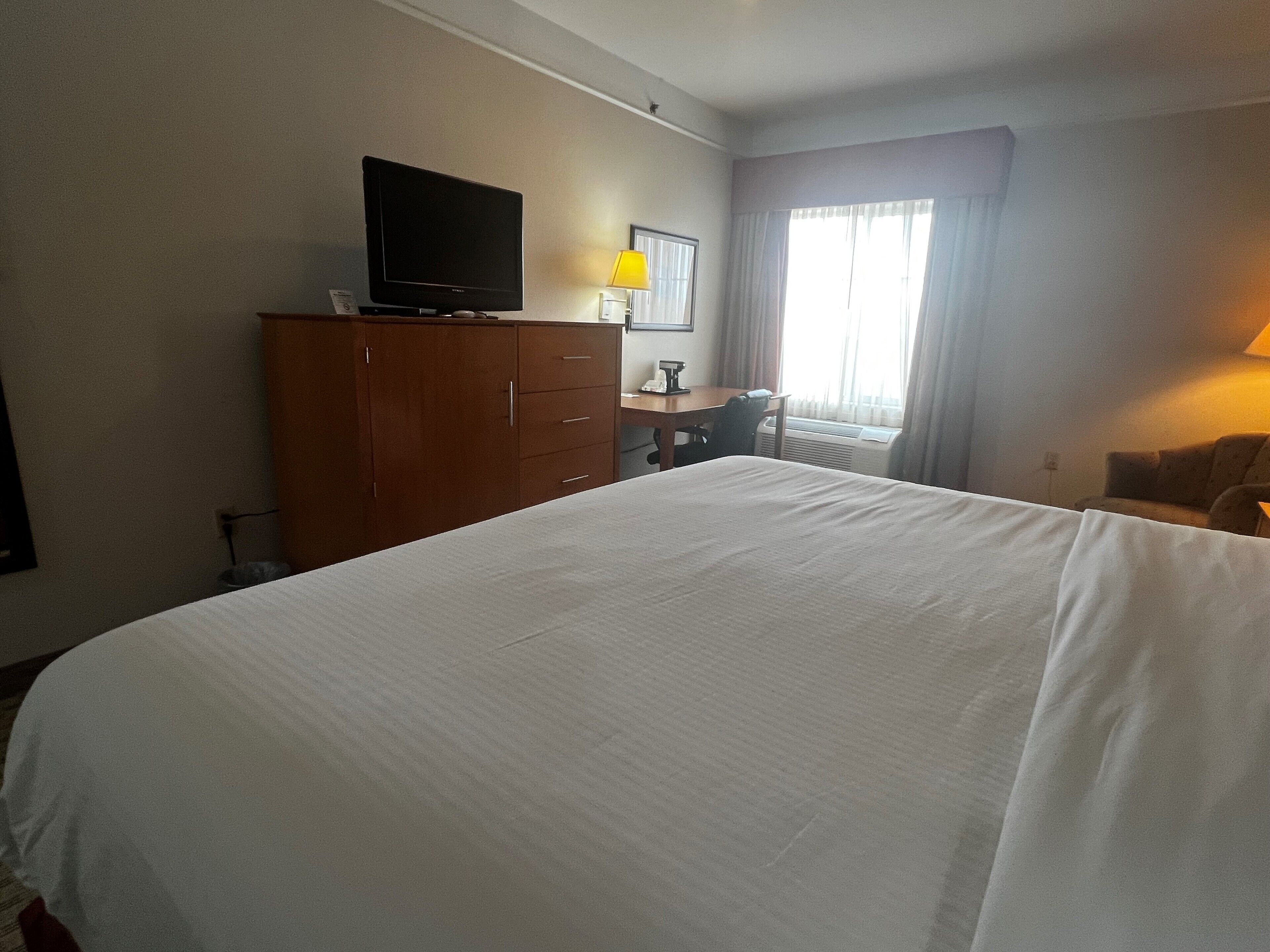 Een hotelkamer met een groot bed, een bureau met stoel, een televisie op een houten kast en een raam met gordijnen.