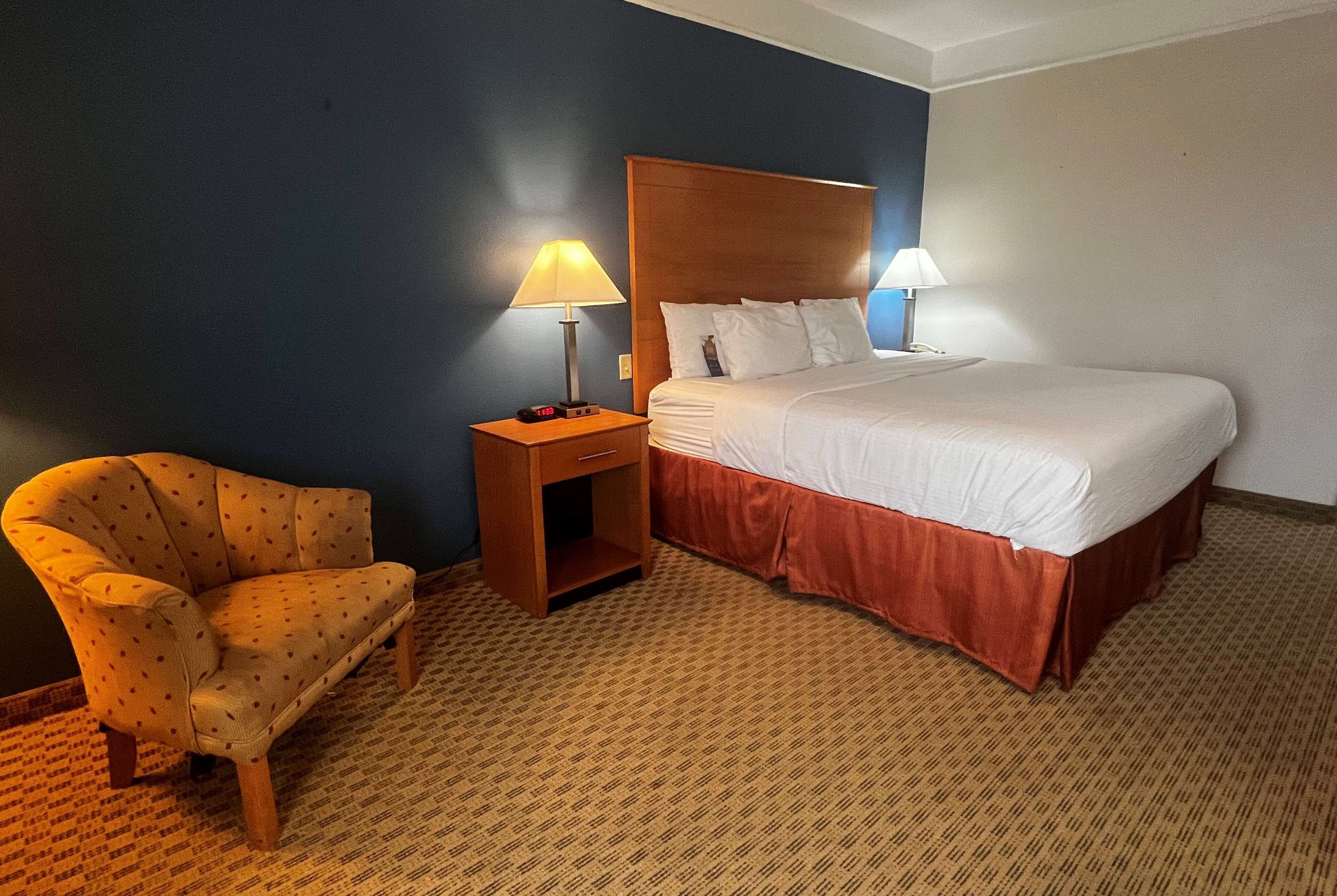 Una habitación de hotel con una cama, una silla y dos lámparas de noche.