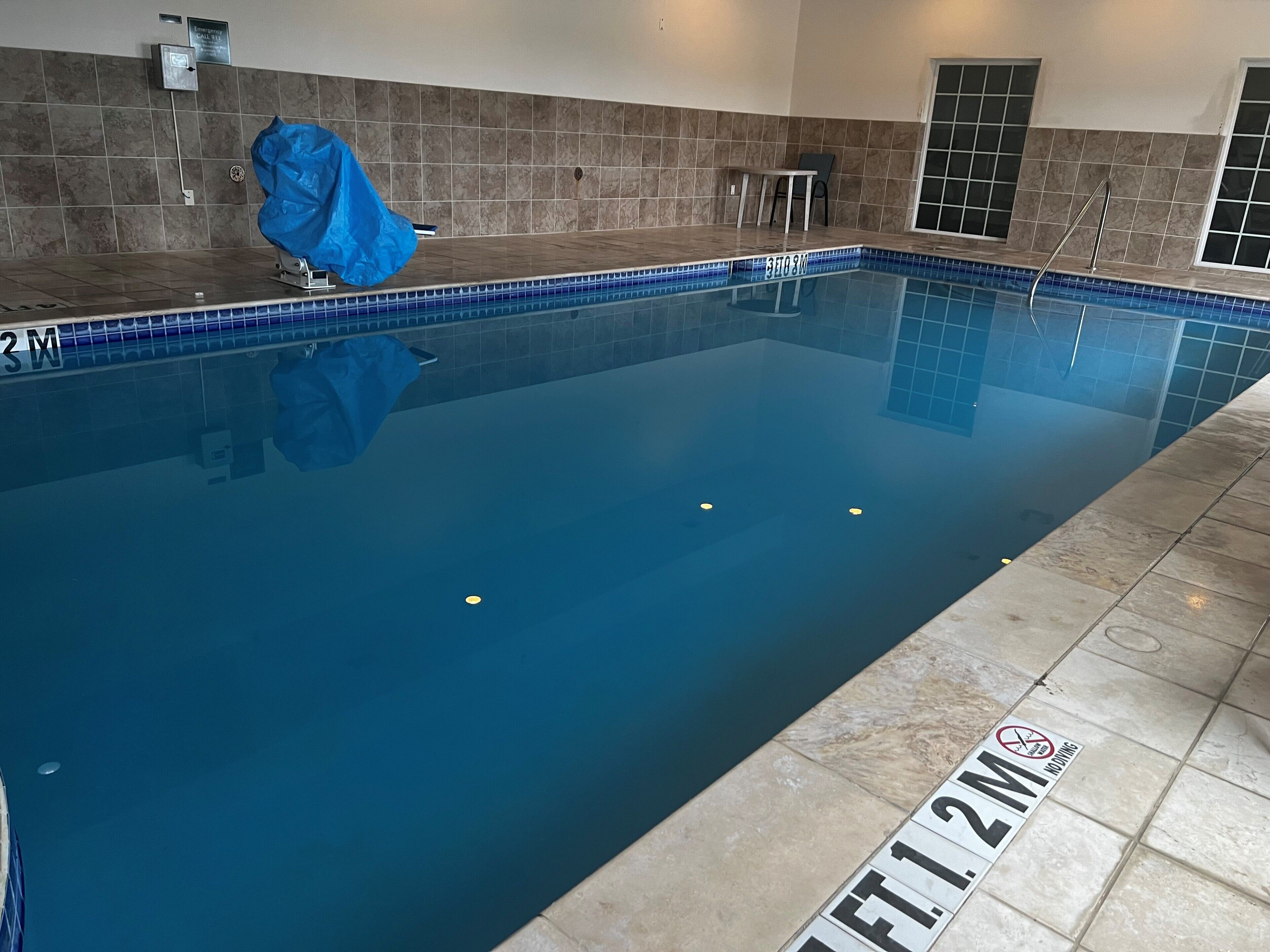 A swimming pool with a tiled edge, a depth marker, and a covered chair.