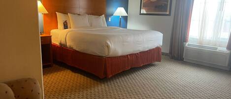 Una habitación de hotel con una cama grande, dos mesitas de noche, una silla, un cuadro en la pared y una ventana con cortinas.