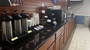 Un comptoir pour le petit-déjeuner avec des distributeurs de café, une machine à café et un tableau affichant le menu.