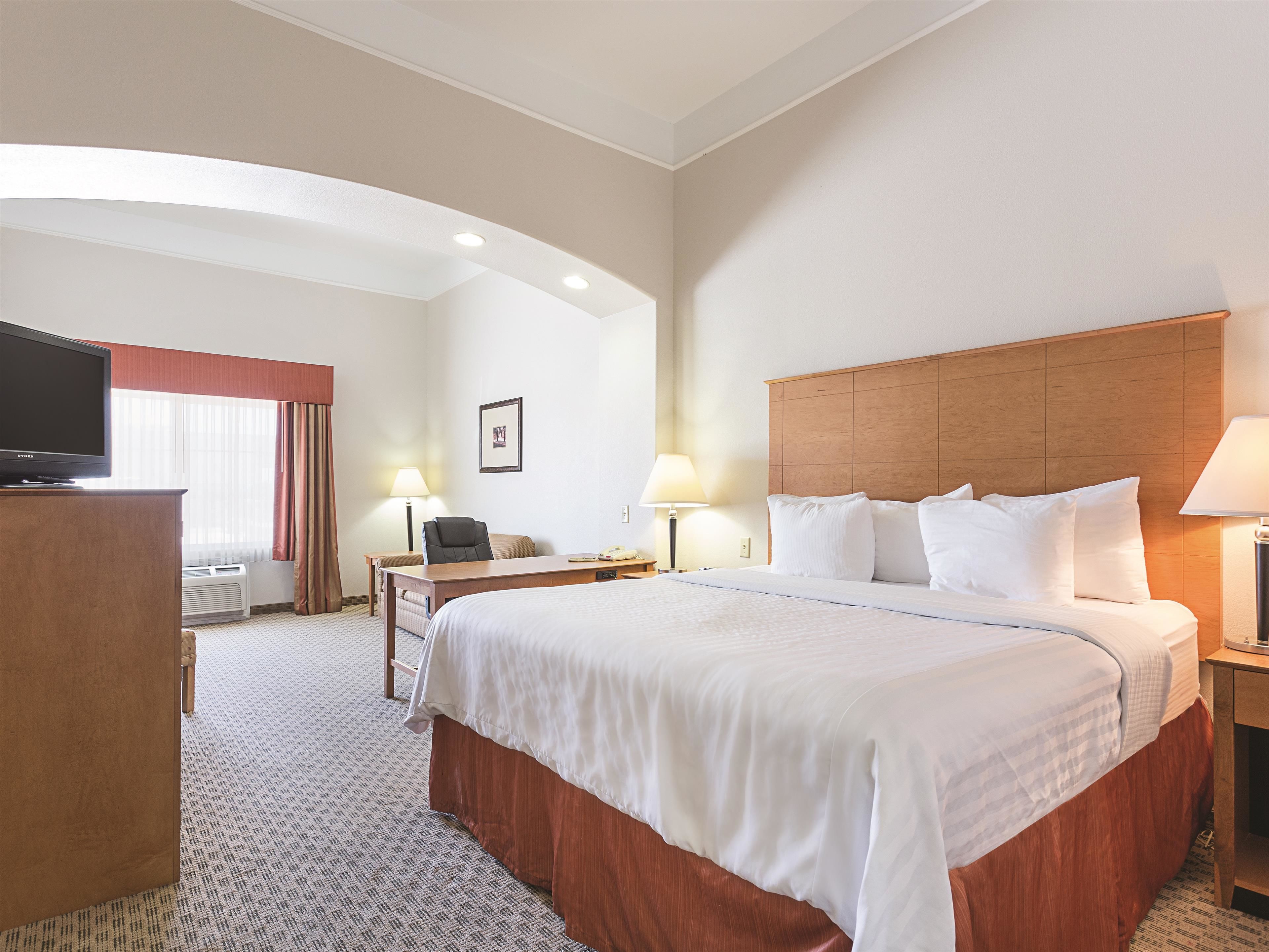 A hotel room with a large bed, a desk, a chair, a television, and a window with curtains.