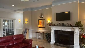 Un salon avec un canapé en cuir rouge, une cheminée, un téléviseur fixé au mur et des appliques murales.