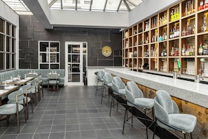 Zona de bar moderna con taburetes altos, mostrador de bar y estanterías llenas de botellas.