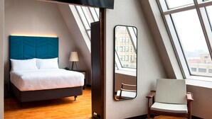 Een moderne hotelkamer met een bed, een stoel, een grote spiegel en uitzicht op de stad door een dakraam.