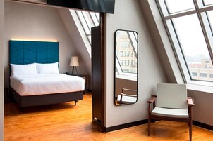 Una habitación de hotel moderna con cama, una silla, un espejo grande y vistas de la ciudad a través de un tragaluz.