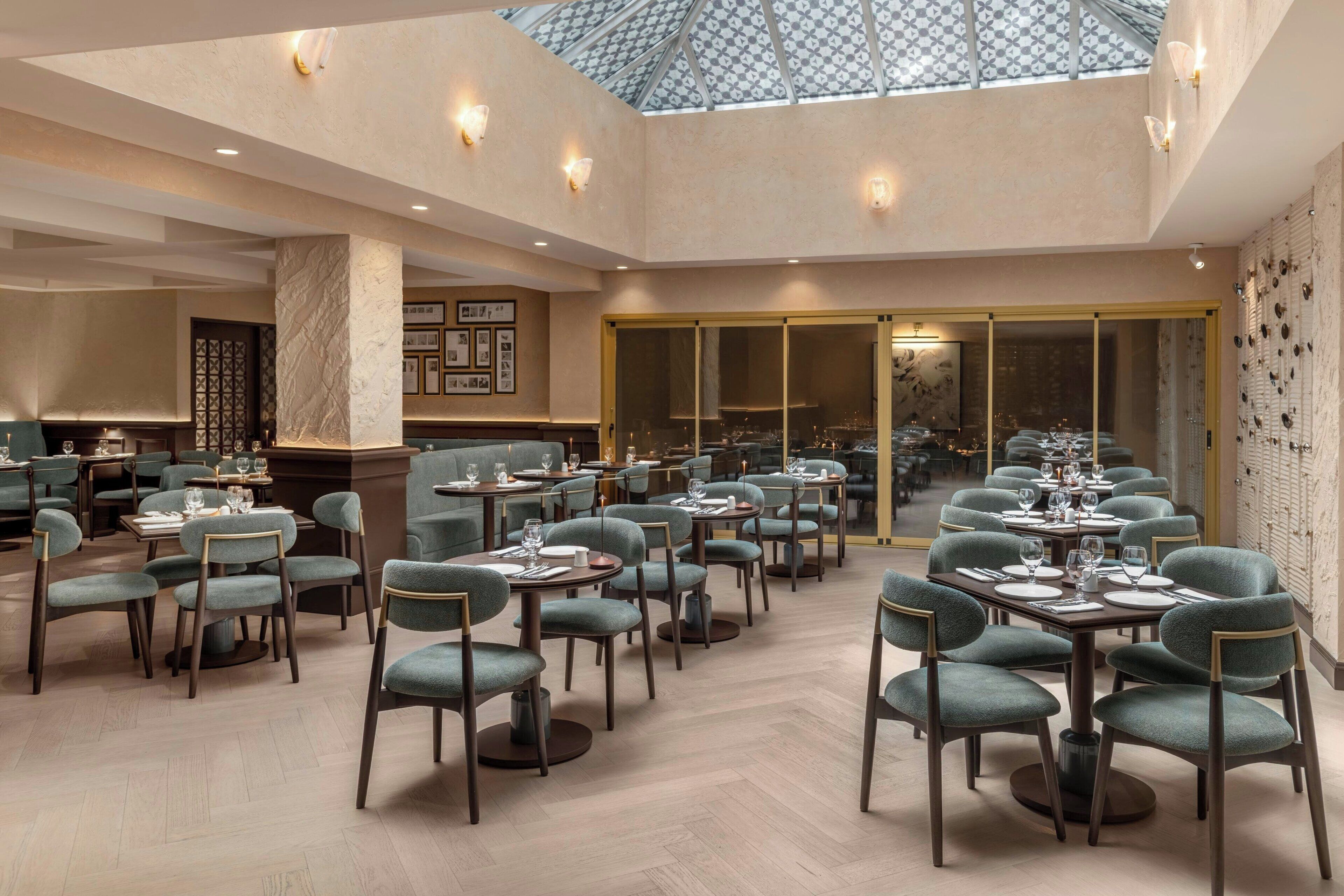 En rummelig restaurant med højt til loftet, ovenlys og udsigt over byen. Bordene er dækket med stole og service.