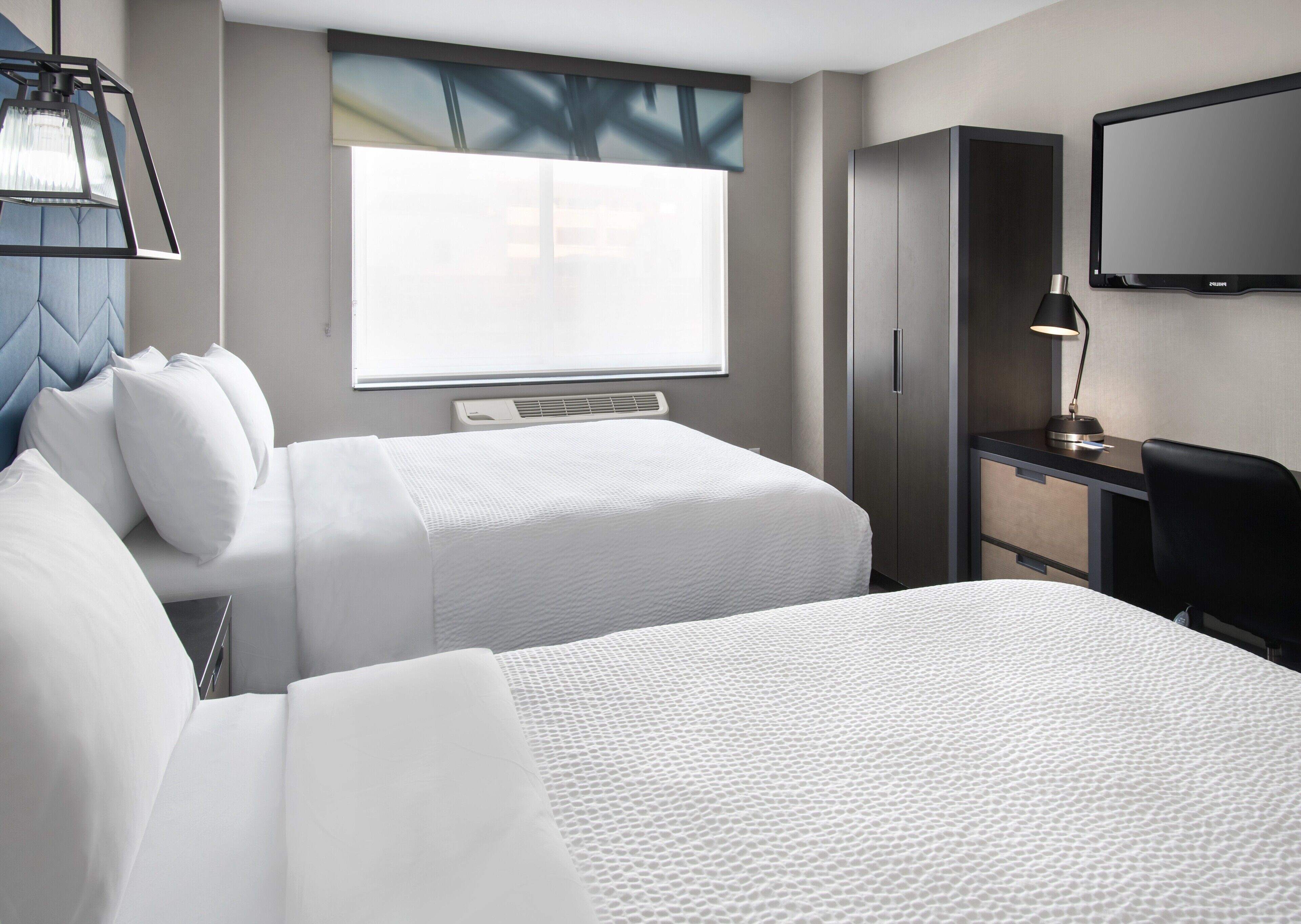 A hotel room with two beds, a desk, a chair, a TV, and a window with blinds.