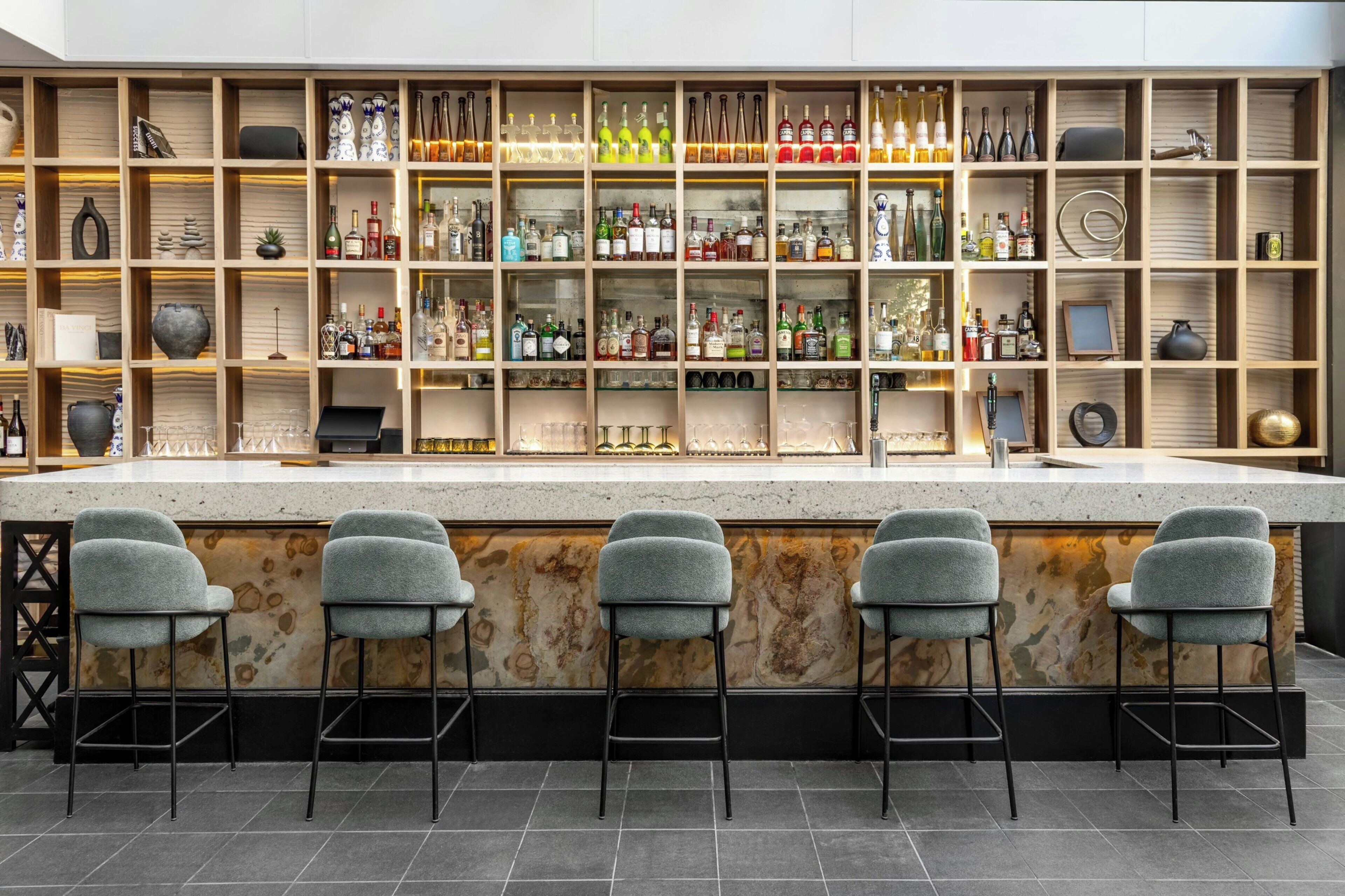 A bar area with multiple shelves of bottles, a counter, and bar stools.