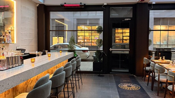 Een moderne bar met glazen dak, barkrukken en een toonbank met flessen en glazen.