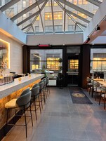 A modern bar area with a glass ceiling, bar stools, and a counter with bottles and glasses.