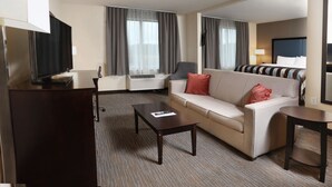 Habitación de hotel con sofá, mesa de centro, televisor y televisor de pantalla plana montado en la pared.