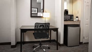 A hotel room with a desk, chair, microwave, refrigerator, and a mirror on the wall.