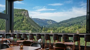 Um restaurante com mesas e cadeiras, grandes janelas com vista para uma paisagem montanhosa.