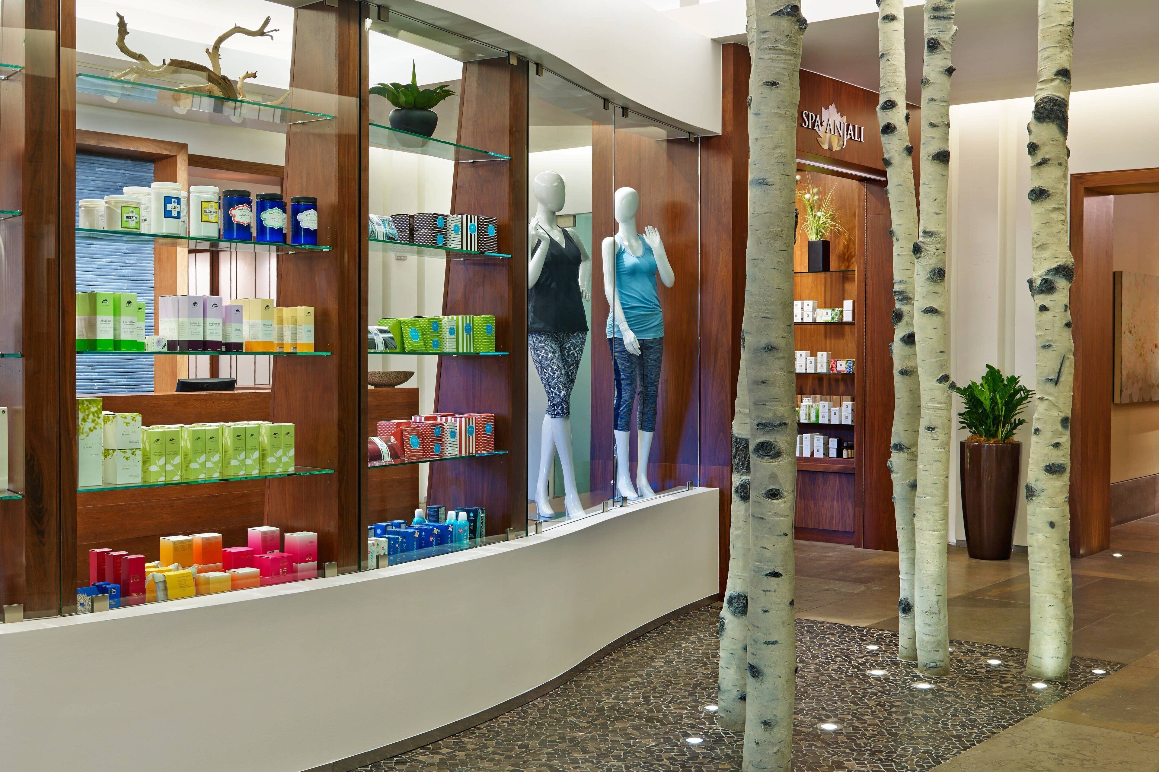Spa- og wellnesscenter med reception, træhylder med forskellige produkter og to mannequiner i badetøj.