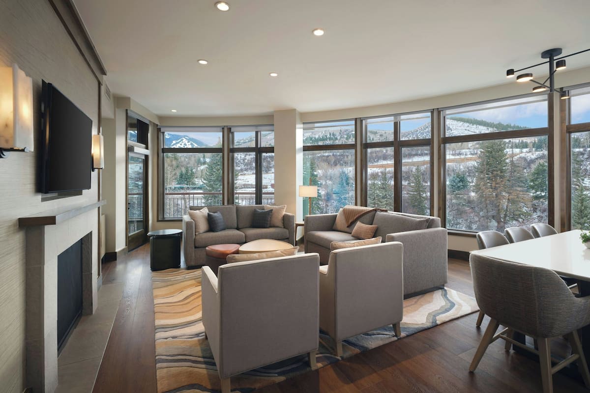 A spacious living room with a fireplace, large windows offering a mountain view, and a dining area with a table and chairs.
