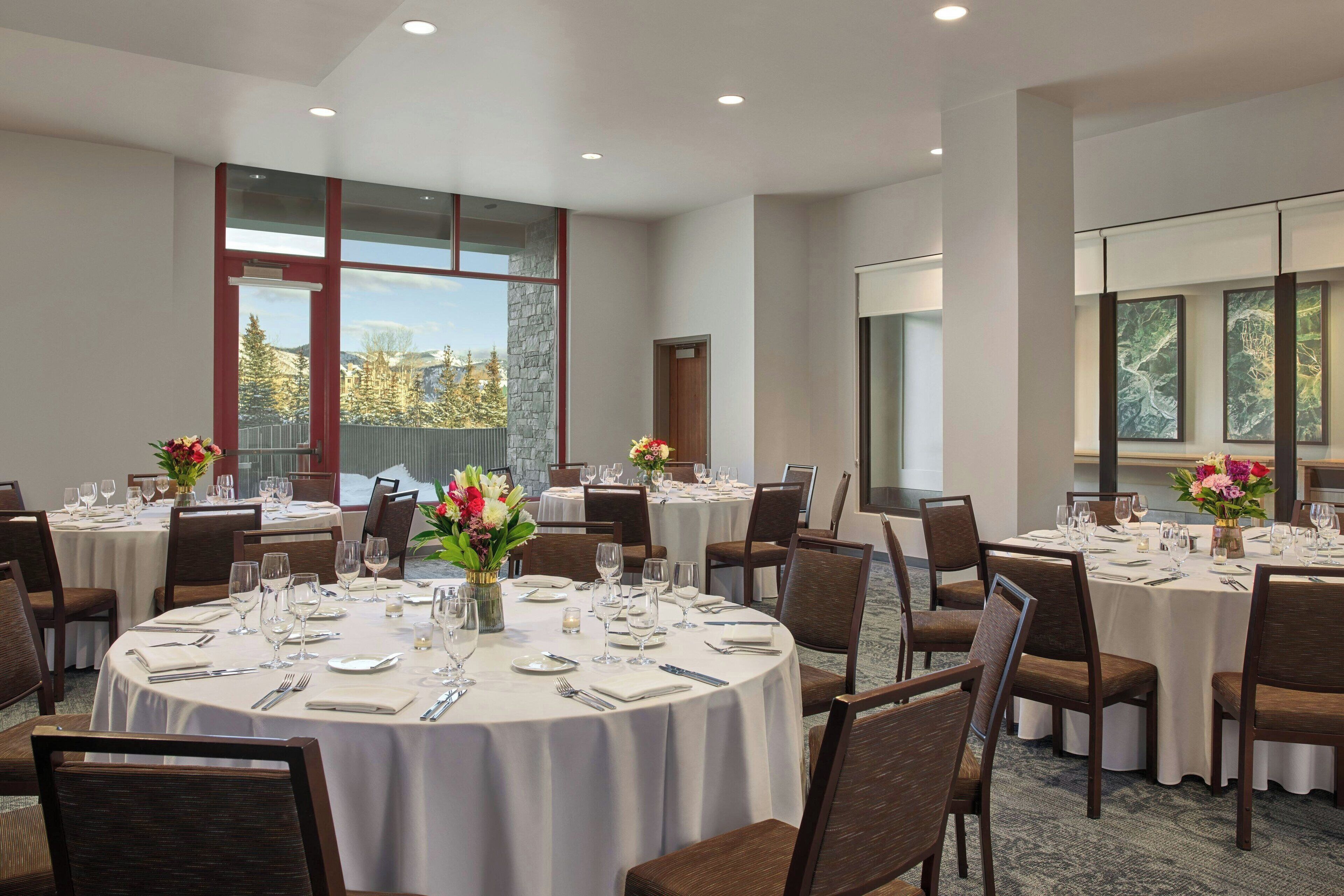 Un salón de conferencias con varias mesas redondas dispuestas para comedor, equipado con sillas y cubiertos.