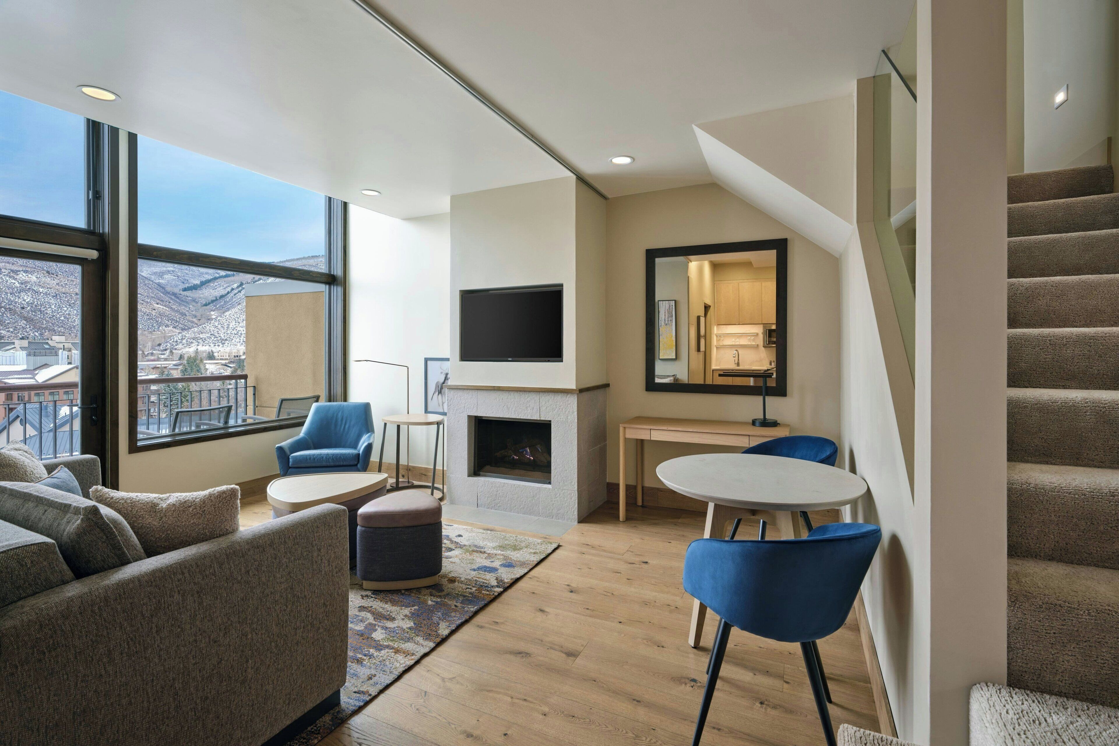 Ein modernes Wohnzimmer mit Kamin, Flachbildfernseher, Essbereich und einer Treppe.