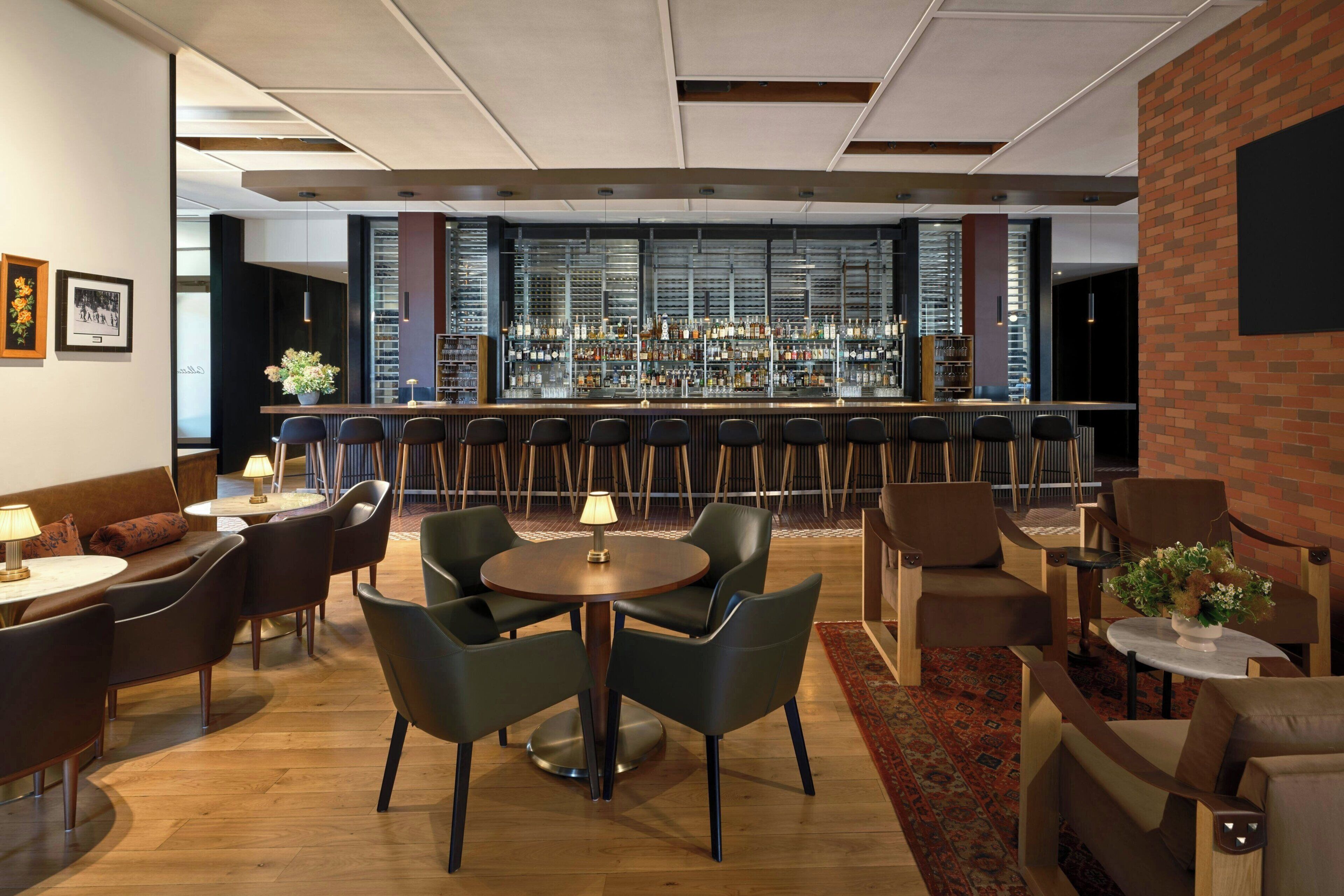 A bar area with a long counter, multiple seating options including round tables and chairs, and a brick accent wall.