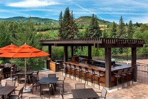 An outdoor patio with a bar area, seating, and a pergola with umbrellas.