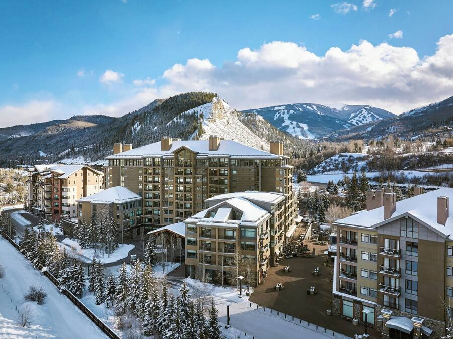 A multi-story hotel with a snow-covered roof, surrounded by mountains and trees.