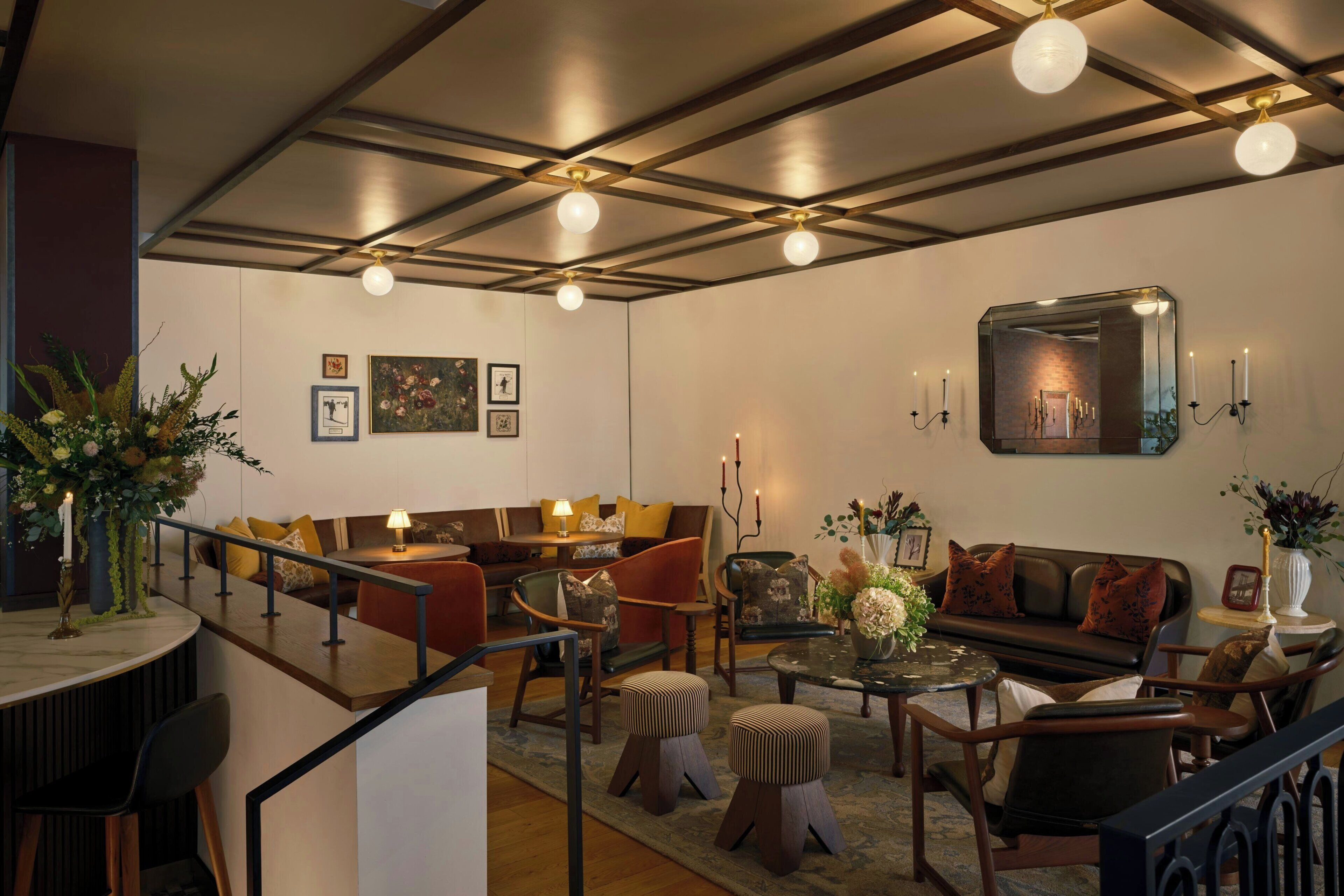 A modern interior with a high ceiling, recessed lighting, a seating area with sofas and chairs, and a small table with a lamp.