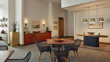 A modern dining area with a wooden table and black wireframe chairs, a kitchen with wooden cabinets, and pendant lighting.
