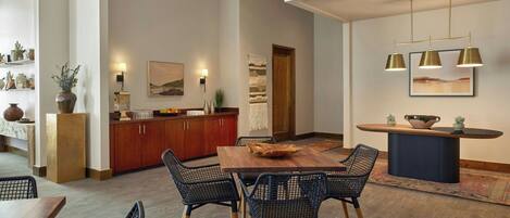 A modern dining area with a wooden table and black wireframe chairs, a kitchen with wooden cabinets, and pendant lighting.