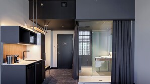 Habitación de hotel moderna con kitchenette, cabina de ducha de vidrio y puerta corredera al baño.