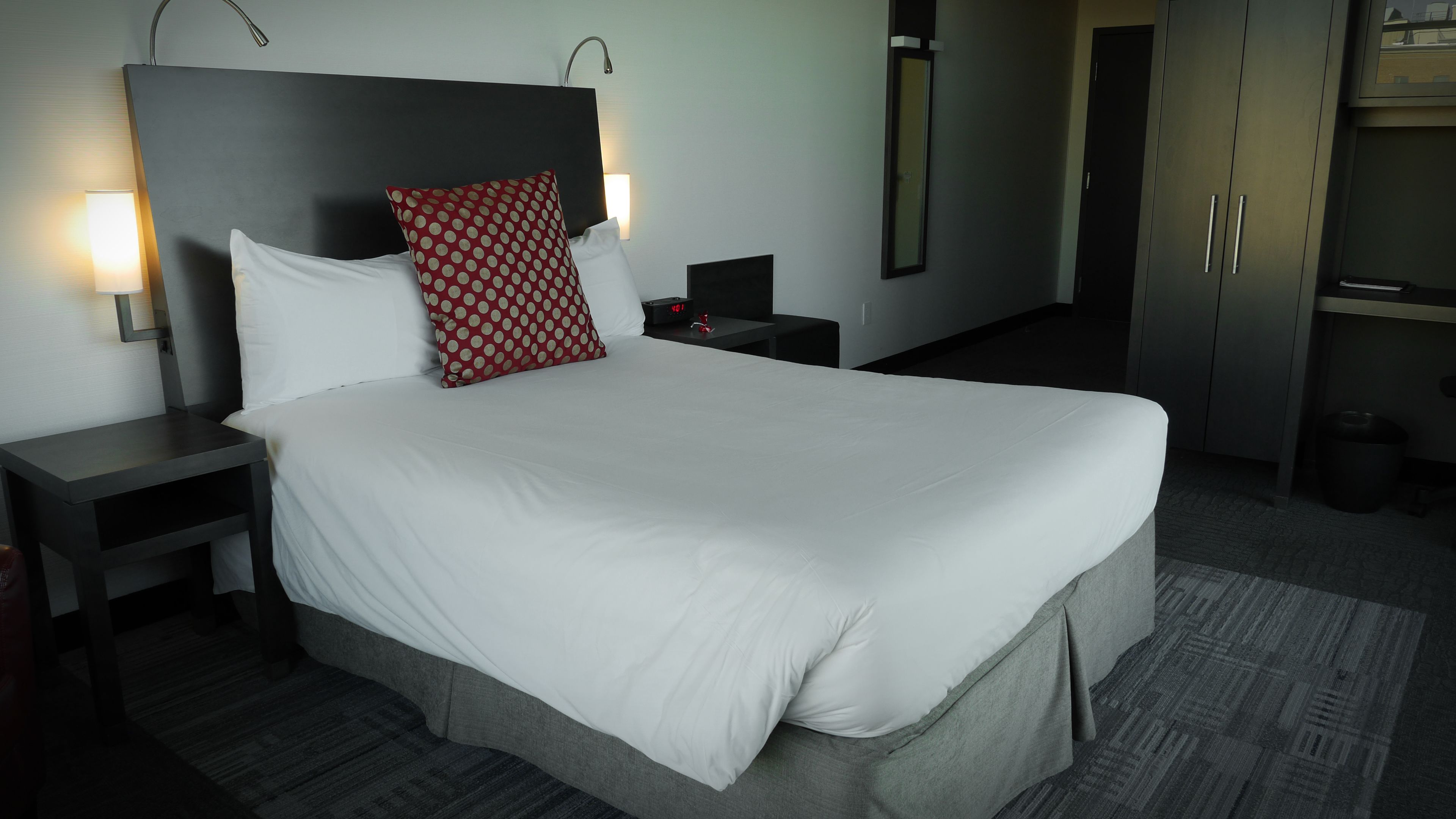 A hotel room with a large bed, a nightstand with a lamp, a wardrobe, and a mirror.