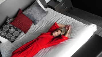 A bed with a white mattress, grey and red pillows, and a red robe.