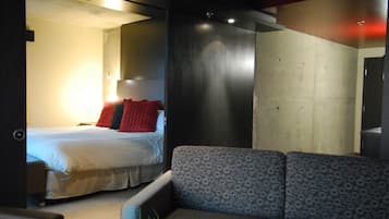 A modern hotel room with a bed, a grey sofa, and a small plant.