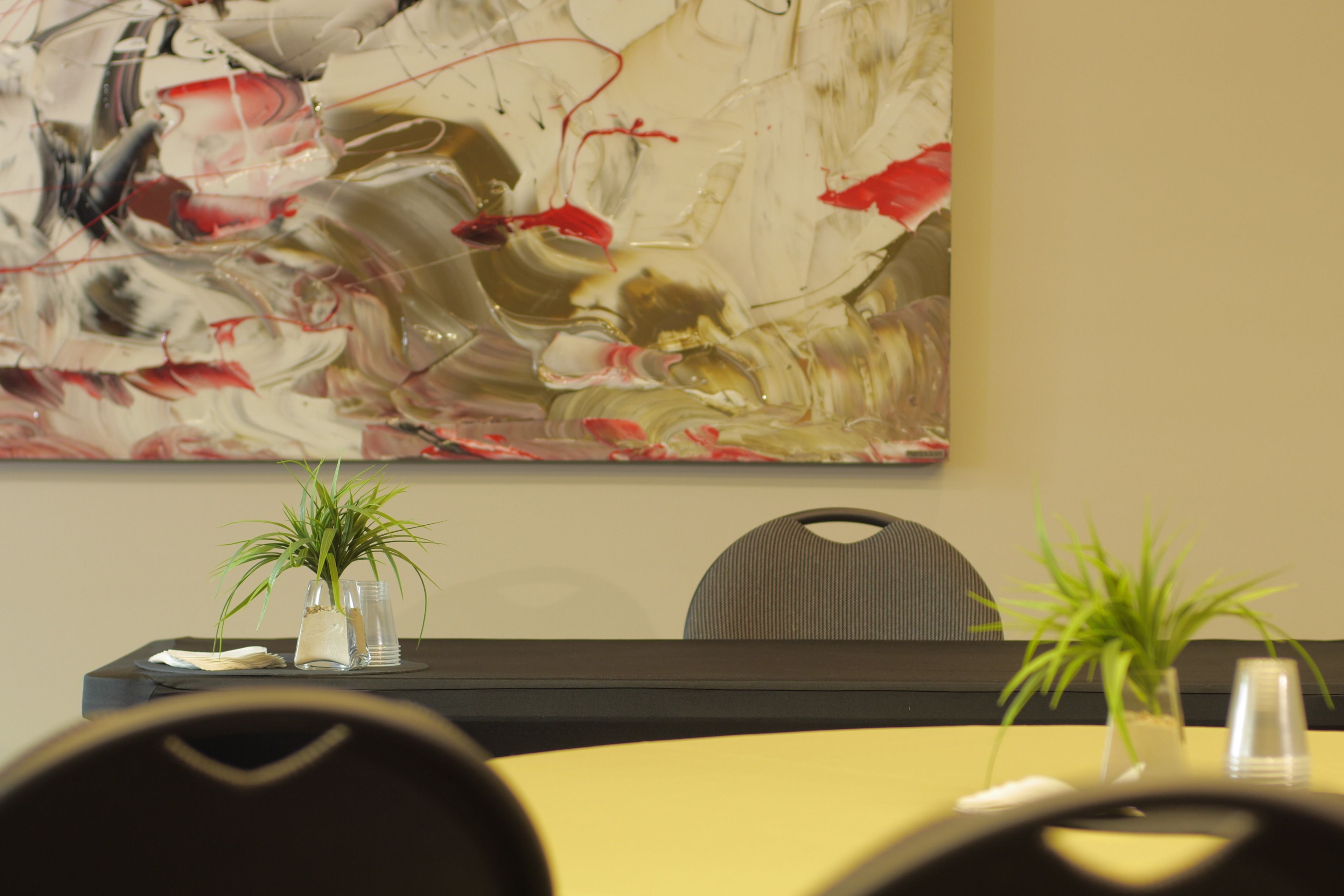 A conference room with a large abstract painting, two potted plants, and a yellow table.