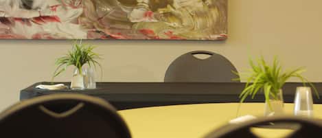 A conference room with a large abstract painting, two potted plants, and a yellow table.