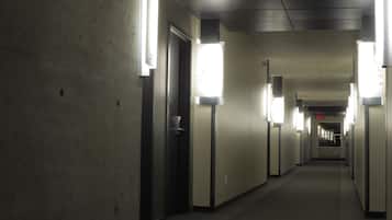 Un pasillo largo y estrecho con iluminación fluorescente, paredes de concreto y puertas a ambos lados.