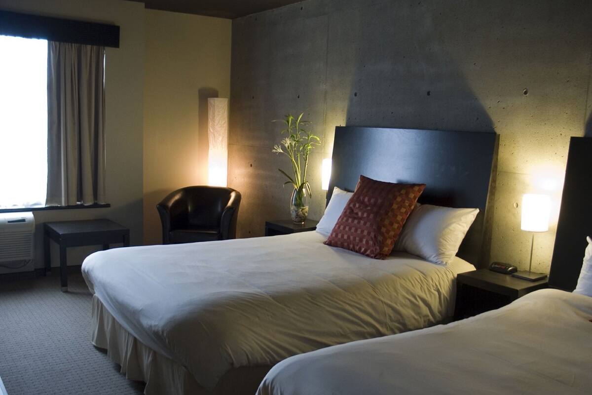 A hotel room with two beds, a chair, a desk, a lamp, and a plant.