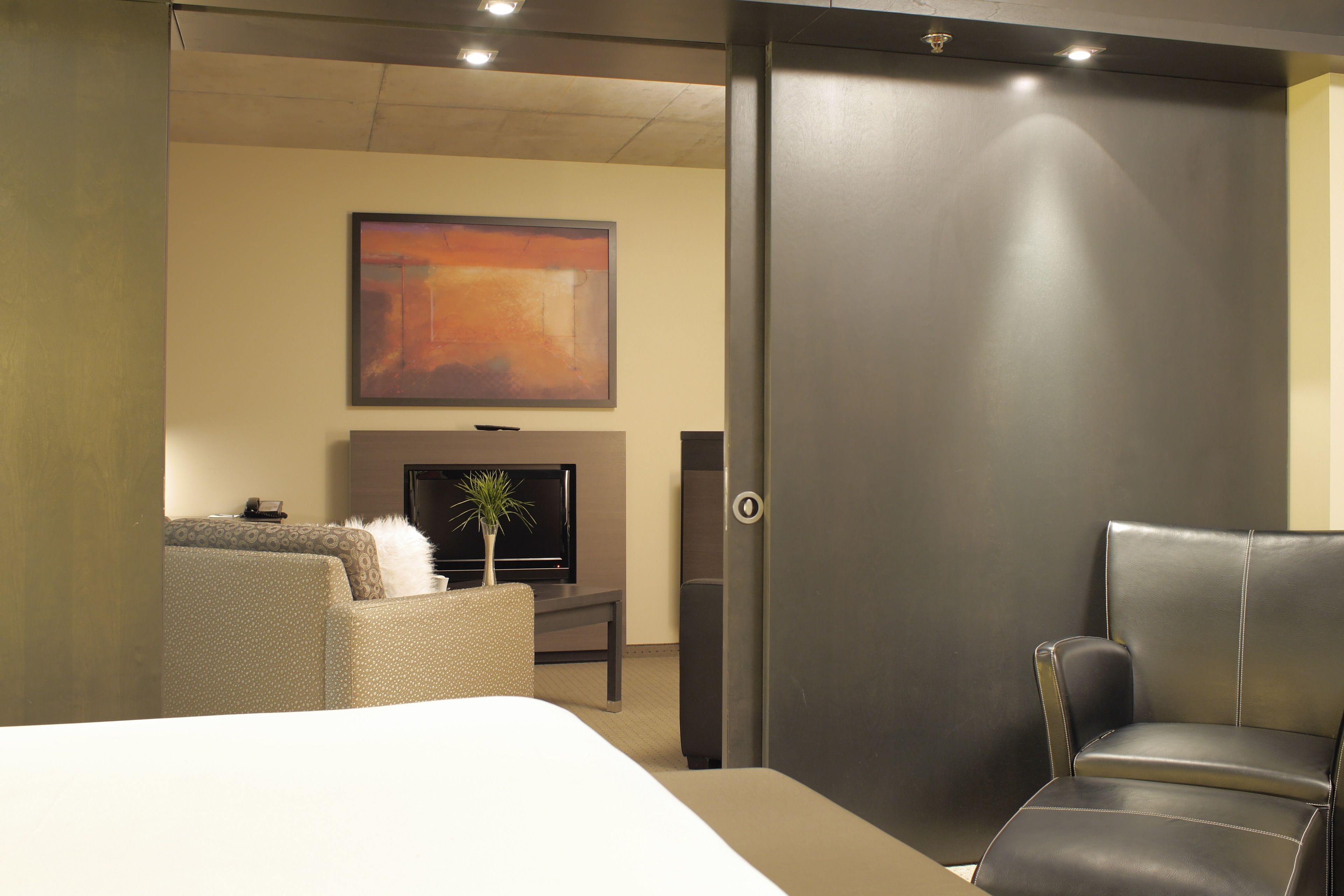 Habitación de hotel con cama, sofá, sillón, televisión y un cuadro en la pared.