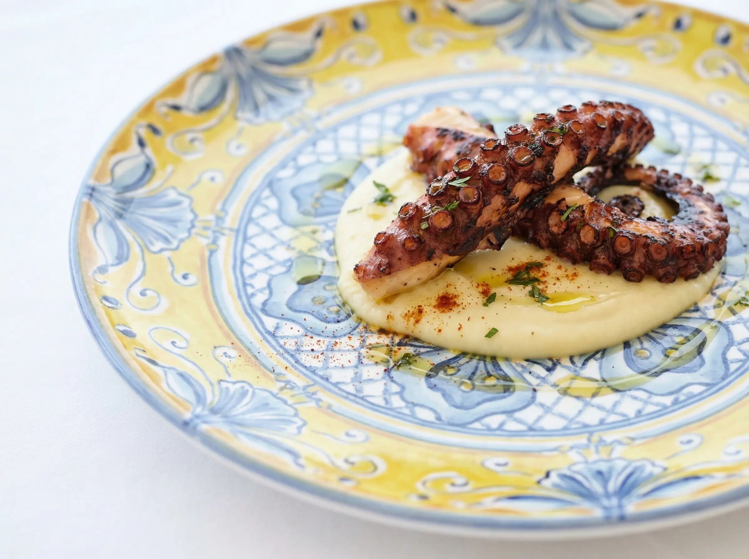 Une assiette contenant des tentacules de poulpe et une sauce crémeuse, le tout présenté sur une assiette en céramique décorative.
