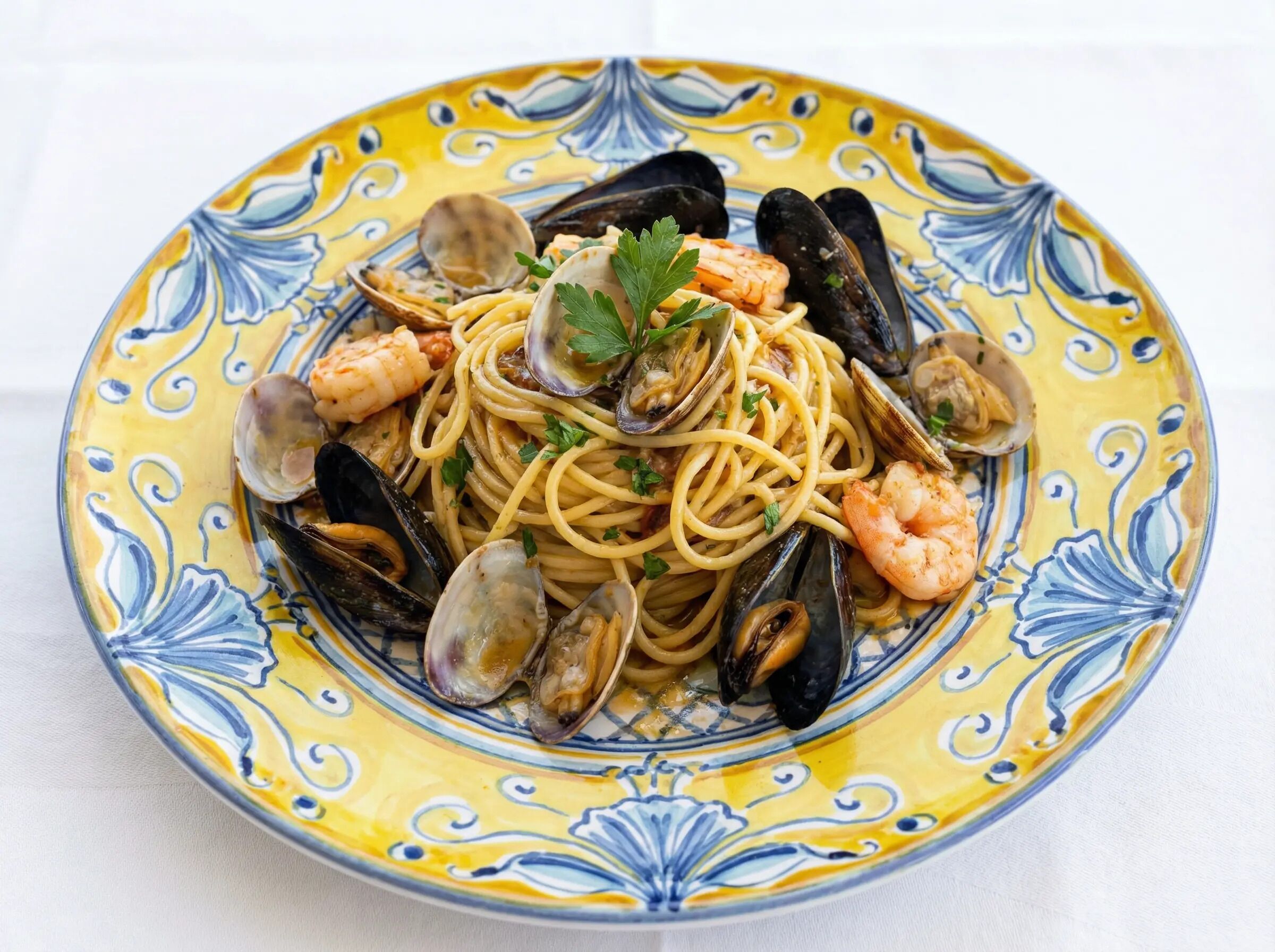 A plate of seafood pasta with mussels and shrimp, garnished with parsley, on a decorative yellow and blue plate.