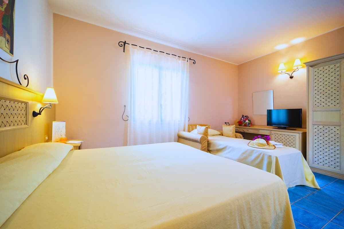 A hotel room with two beds, a television, a desk with a lamp, and a large window with curtains.