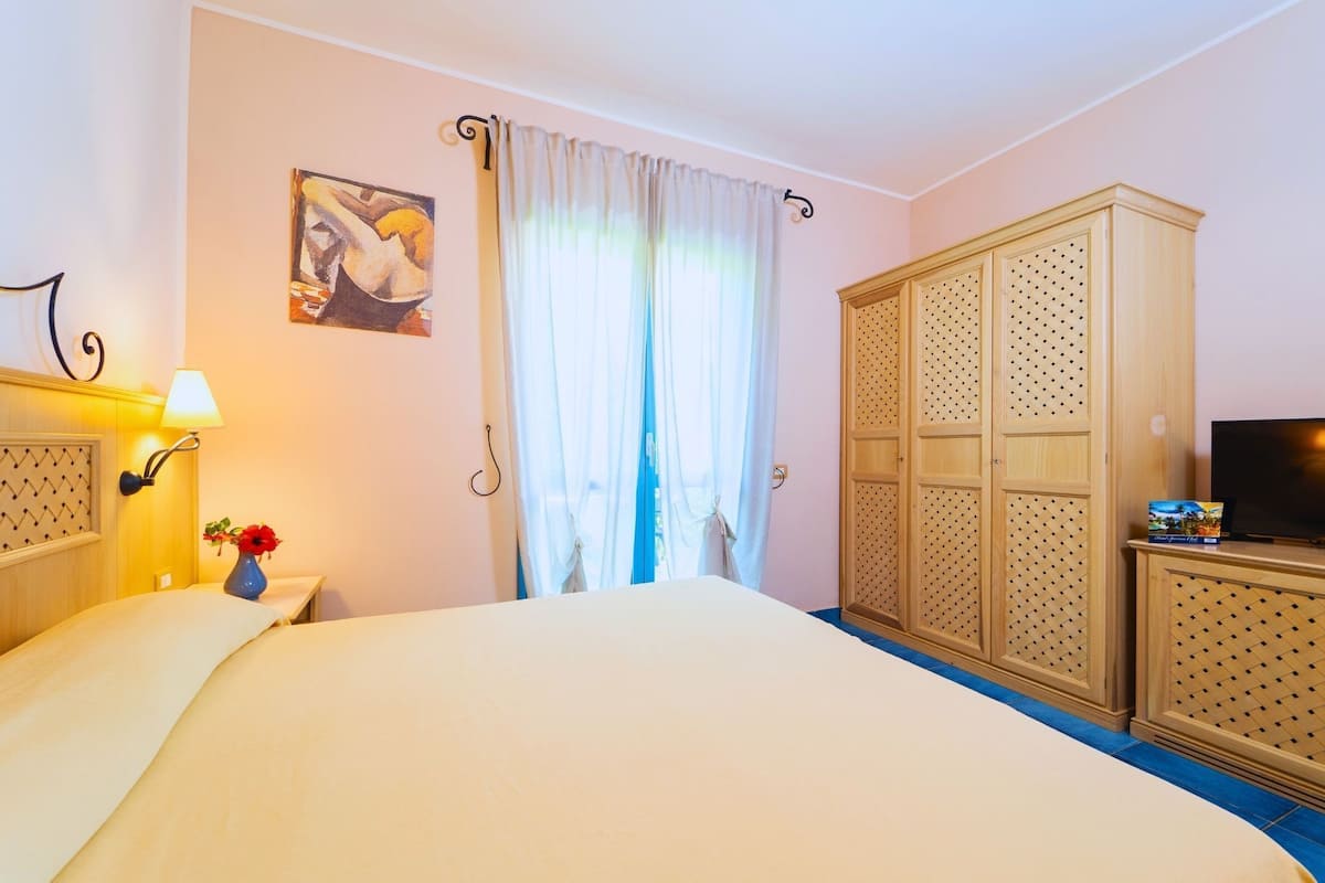 A hotel room with a bed, a TV, a wardrobe, a painting, and a lamp.