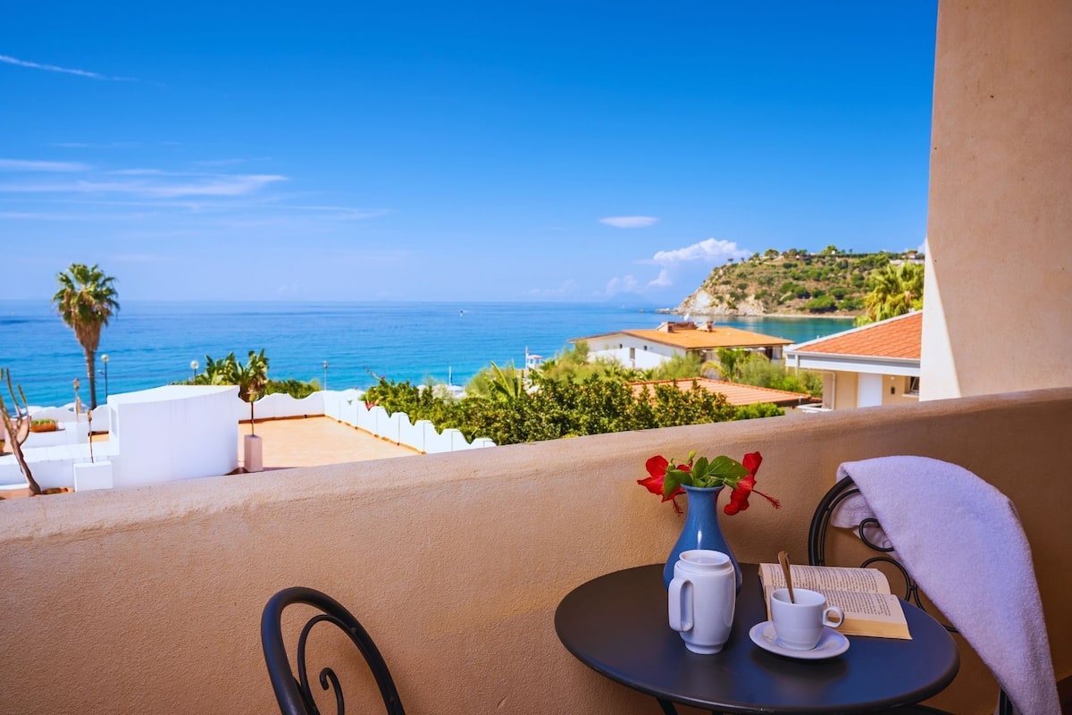 A balcony with a table, a vase with flowers, a cup, and a book.